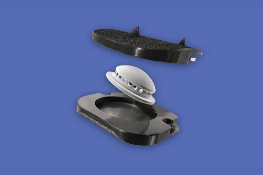An exploded view of a BAGUERA-C cervical artificial disc implant showing the upper and lower anatomical plates and the central mobile nucleus on a blue background.