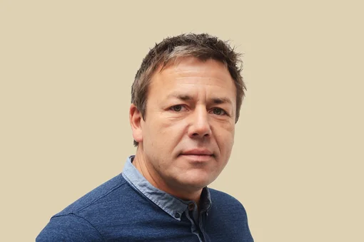 Stephan Warnat, Ceo of ENANDE Headshot of Stephan Warnat, CEO, wearing a blue button-down shirt, set against a brown background.