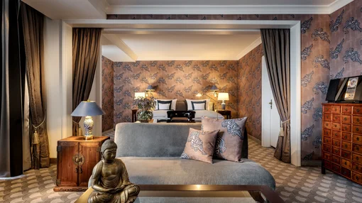 Elegant Junior Suite Living Area A luxuriously decorated suite with tiger-patterned wallpaper, a gray velvet sofa, a Buddha statue, and a glimpse into the bedroom area.