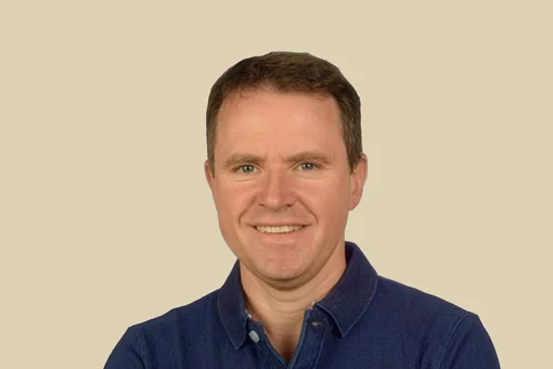 Dr. Gregor Möckel - Medical Professional Professional headshot of Dr. Gregor Möckel, smiling and wearing a navy blue polo shirt, set against a brown background.