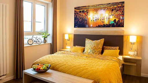 A well-lit deluxe room for solo travelers featuring a large yellow-clad bed, a decorative bicycle on the windowsill, and a vibrant action-shot wall mural.