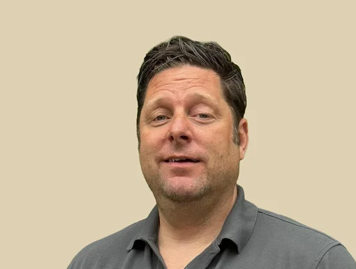 Professional portrait of Dr. Jan Spiller, looking forward with a neutral expression, wearing a grey polo shirt against a brown background.