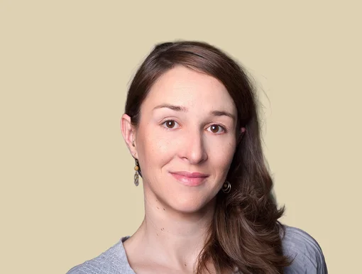 Professional portrait of Nadine Dressler, featuring a friendly expression and long brown hair, wearing a light grey blouse against a brown background.