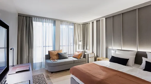 An alternative view of the standard double room showing a flat-screen TV, a leopard-print footstool, and a work desk near the window.