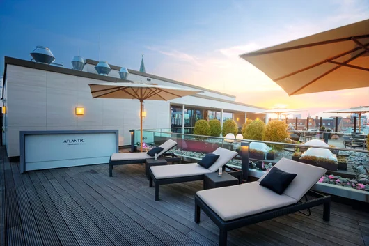 A modern rooftop terrace with lounge chairs, large umbrellas, and a sunset view over the Bremen city skyline.
