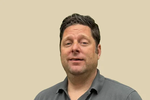 Dr. Jan Spiller - Spine Specialist Professional portrait of Dr. Jan Spiller, looking forward with a neutral expression, wearing a grey polo shirt against a brown background.