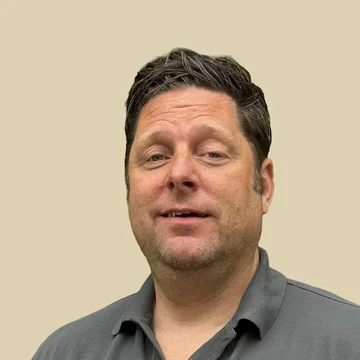 Professional portrait of Dr. Jan Spiller, looking forward with a neutral expression, wearing a grey polo shirt against a brown background.