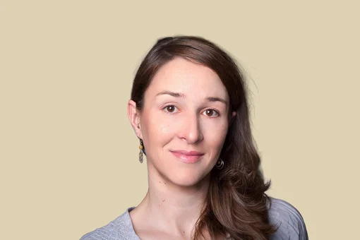 Nadine Dressler - Medical Team Member Professional portrait of Nadine Dressler, featuring a friendly expression and long brown hair, wearing a light grey blouse against a brown background.