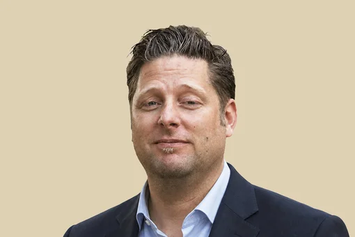 Professional portrait of Dr. Jan Spiller, looking forward with a neutral expression, wearing a grey polo shirt against a brown background.