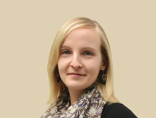 Professional headshot of Corina Silber, an office manager, wearing a patterned scarf and smiling against a brown background.
