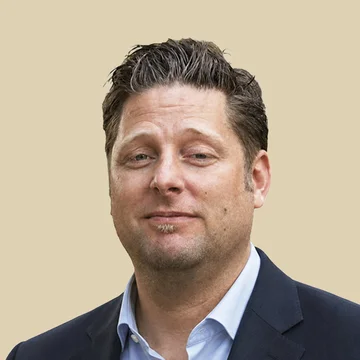 Professional portrait of Dr. Jan Spiller, looking forward with a neutral expression, wearing a grey polo shirt against a brown background.