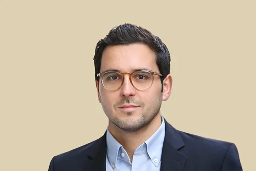 Dr. Nils Farhan, Orthopedic Surgeon and Shoulder Specialist Headshot of Dr. Nils Farhan with short dark hair, wearing glasses, a light blue button-down shirt, and a dark blazer, set against a solid beige background.